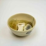 A top-down look at this small stoneware bowl. The stoneware is a ceram-coloured base painted with various abstract designs in shadesof blue, khaki, beige, and brown