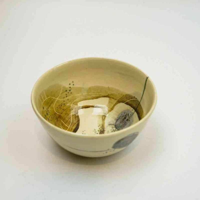 A top-down look at this small stoneware bowl. The stoneware is a ceram-coloured base painted with various abstract designs in shadesof blue, khaki, beige, and brown