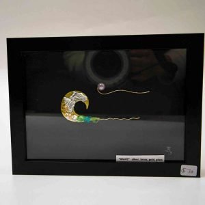 A black frame holding a silver sculpture of a wave. The piece is minimal, just one wave in the centre of the frame.