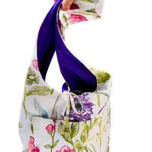 A large white bag with a floral pattern is held up in front of a white background. The interior deep purple peaks out.