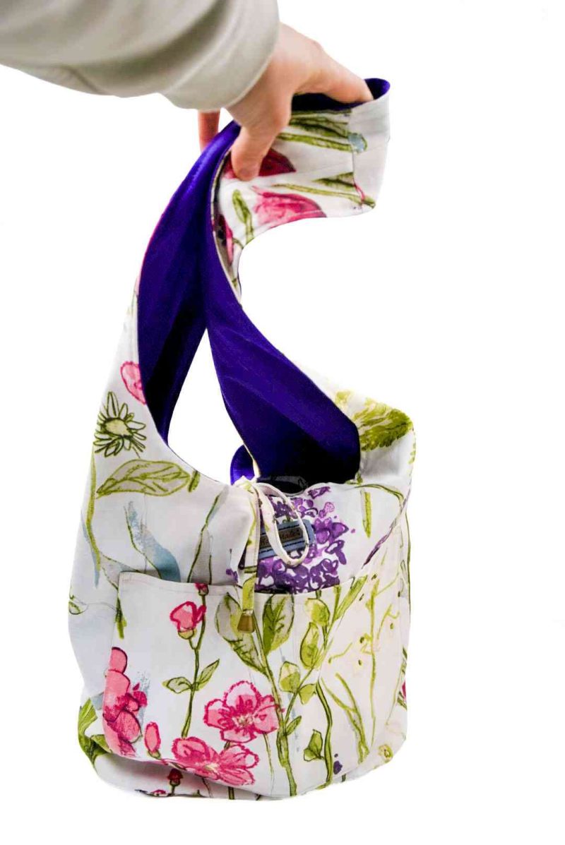 White floral bag purple lining (2) A large white bag with a floral pattern is held up in front of a white background. The interior deep purple peaks out.