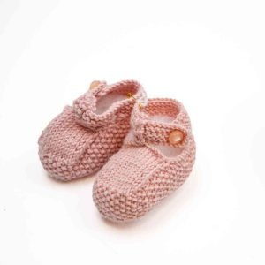 A pair of knitted baby shoes in a soft pink colour with a button on the side.