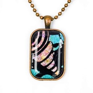 A Large rectangular pendant hangs on a copper-toned chain, resting against a white background. The pendant is made up of a copper-toned frame filled with resin. The resin is clear and covers an abstract design consisting of a black base, and an opalescent, peach-coloured conical shape resembling a spire shell