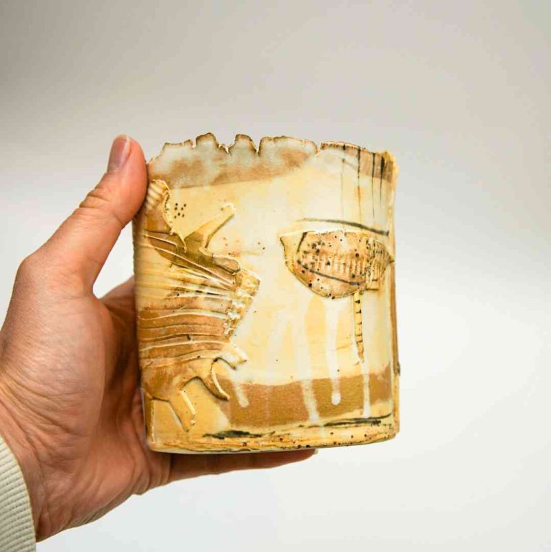 stoneware vase beige Magda (2) A short, sand-tned, stoneware vase is held in the hand of a fair-skinned woman against a white background