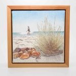 Big K- Port Beach (1) Framed ballpoint pen drawing of a beach scene showing rocks and grass in the foreground, with a person walking along the shoreline under a clear blue sky.