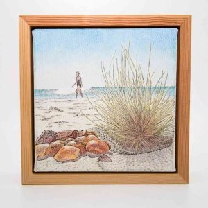 Framed ballpoint pen drawing of a beach scene showing rocks and grass in the foreground, with a person walking along the shoreline under a clear blue sky.