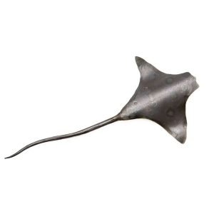 A metal sculpture of an eagle ray lays on an all white background. The ray is made of a dark metal and has some subtle circles on the back to resemble an eagle ray
