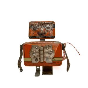 Small robot sculpture made from orange vintage tins, metal hinges, and brackets with a rustic finish.