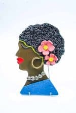 A stoneware Wall hanging piece depicting a dark-skinned woman wearing a blue shirt with pink flowers in her hair